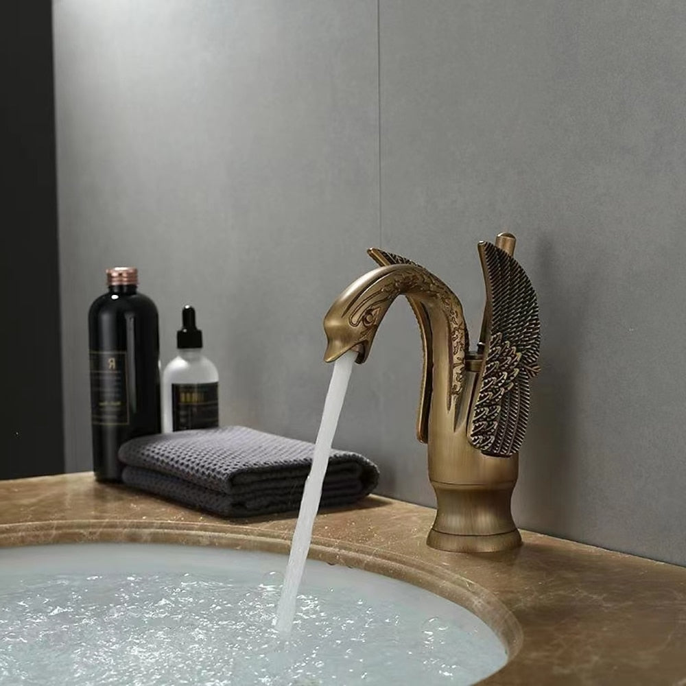 Bronze faucet with water flowing into a sink, with bottles and a towel in the background.